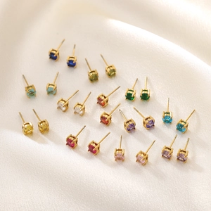 Gros plan de 12 paires de boucles d'oreilles en zircone colorée sur tissu de soie blanc