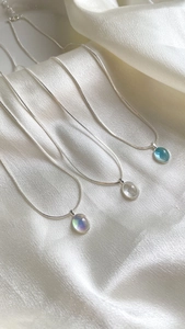 Detailed view of three minimalist oval necklaces on white silk with silver snake chains