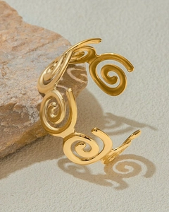 Dettaglio di un bracciale aperto dorato a spirale appoggiato su una base di pietra naturale