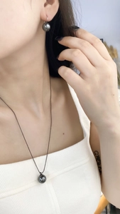 Detail of luxury dark pearl jewelry set featuring necklace and earrings on model