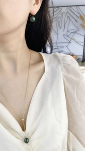Detail of elegant dark green pearl drop earring and gold necklace on model