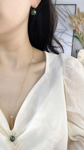 Detail of dark green pearl necklace and earrings set with 18k gold finish on a model