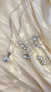Detailed view of silver-gray pearl necklace and earring set on yellow satin fabric