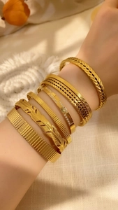 Close-up of stacked gold vintage cuffs including feather and pleated textures on model