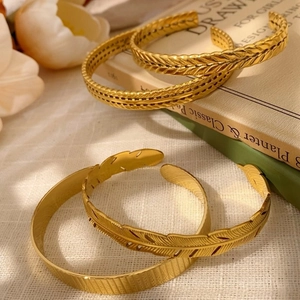Set of four vintage gold open bracelets with leaf and feather patterns on retro book