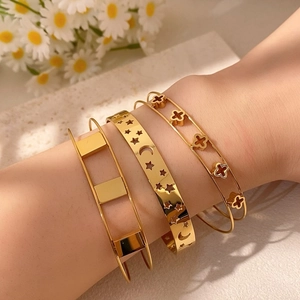 Dettaglio di bracciali dorati sovrapposti con design a stella, luna e quadrifoglio