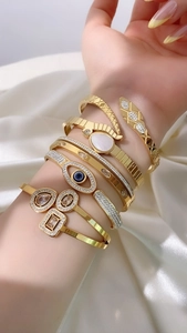 Close-up of gold layered bracelets with snake head and devil eye details on white satin