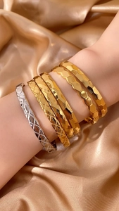 Dettaglio di sei bracciali geometrici oro e argento su raso color champagne