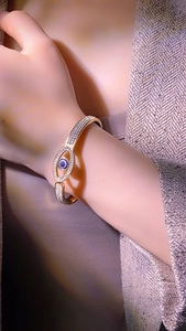 Detail shot of a golden spring snake bracelet featuring a crystal-encrusted evil eye motif