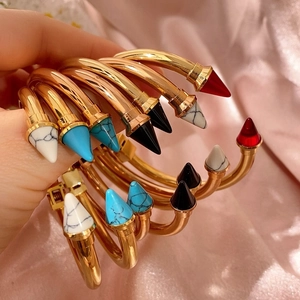 Elegante bracciale rigido dorato aperto con punte coniche colorate su seta rosa