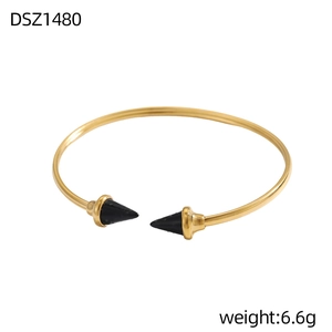 Dettaglio del bracciale rigido dorato con punte a cono nere e finitura minimalista
