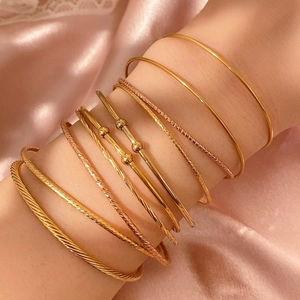 Nahaufnahme gestapelter goldener und roségoldener Kugelarmbänder auf rosa Seide