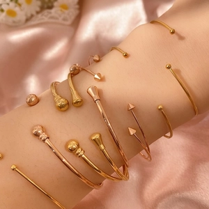 Stapelbares Armreif-Set mit Roségold-Kugeln und Kegelenden auf rosa Seidenhintergrund