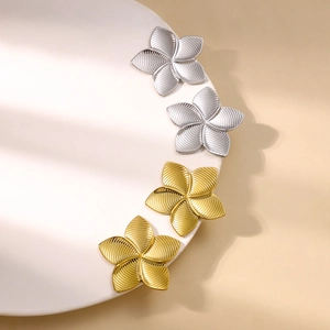 Minimalist gold and silver five-petal flower stud earrings with radial texture on a white plate