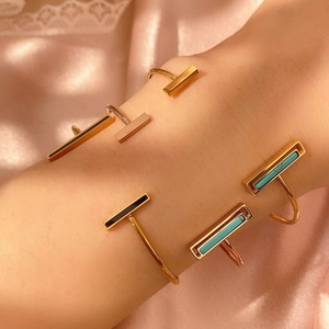 Nahaufnahme goldener geometrischer Armreifen mit Emaille-Inlays auf rosa Seidenstoff