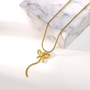 Detail of golden bow pendant with snake chain tassels on white marble surface
