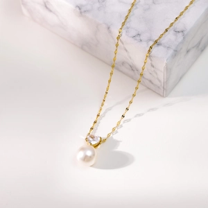 Detail of heart zircon and pearl pendant on a gold chain against marble background