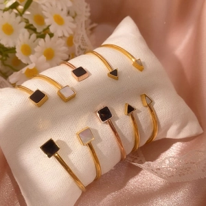 Dettaglio di bracciali rigidi dorati con intarsi geometrici in pietra bianca e nera