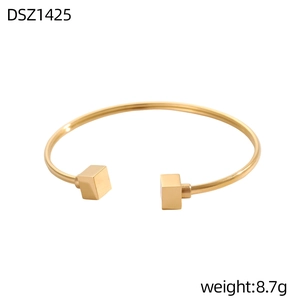 Dettaglio di un bracciale rigido dorato geometrico con estremità a cubo lucido