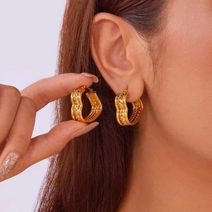 Exaggerated golden hoop earrings with textured weave pattern on a model