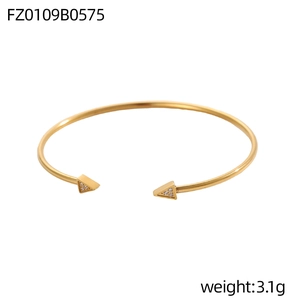 Dettaglio di un bracciale rigido dorato con punte geometriche e cristalli incastonati