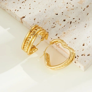 Detail of chunky C-shaped golden earrings with braided texture on a stone background