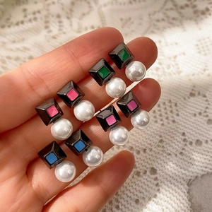 Detalle de pendientes geométricos con esmalte de colores y perlas sobre encaje blanco