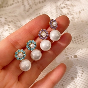 Detalle de pendientes de flores en rombo con perlas blancas grandes y base dorada