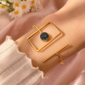 Brazalete geométrico dorado con marco rectangular y piedra azul sobre tela rosa suave
