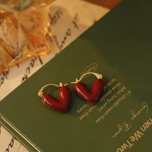 Dettaglio di orecchini a cuore rosso con ganci dorati su un libro d'epoca verde