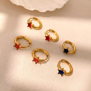 Set of six gold hoop earrings with red and blue star-shaped gemstones on white surface