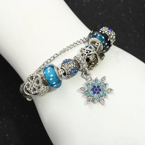 Detail of silver snake chain bracelet featuring blue glass beads and snowflake charm pendant