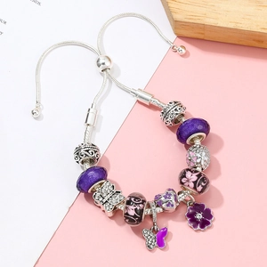 Detail eines lila Charm-Armbands mit Schmetterlings- und Blumenanhängern an Silberkette
