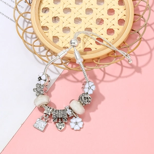 Verstellbares silbernes Charm-Armband mit weißen Blumen- und Herzanhängern vor Rosa