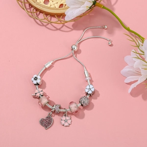 Details eines silbernen Kettenarmbands mit rosa Blumenanhängern und Herz-Kristallanhänger