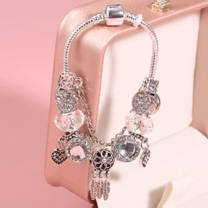 Silver snake chain bracelet featuring heart charms and dreamcatcher pendant on a pink box