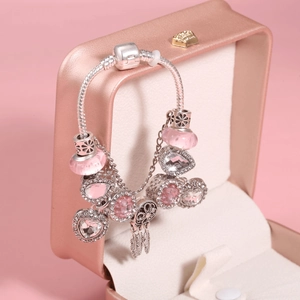 Detail of pink charm bracelet featuring dreamcatcher and heart charms on a jewelry box