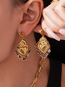 Detailed close-up of gold heart earrings with colorful stones and baroque metal texture