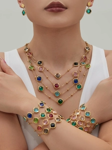 Detail von mehrlagigen Goldketten und Armbändern mit bunten facettierten quadratischen Steinen