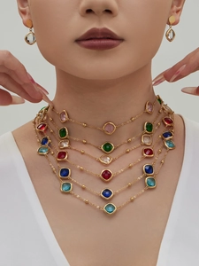 Details einer mehrlagigen goldenen Edelstahlkette und Ohrringen mit bunten Glassteinen