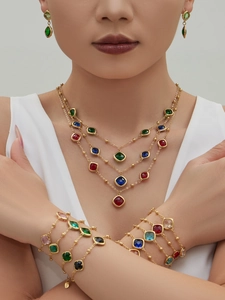 Close-up of a layered gold necklace and bracelets featuring colorful square-cut gemstones