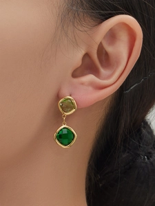 Detail of model wearing double-layered gold earrings with square green glass stones