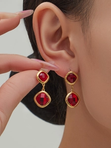 Detail of red geometric glass crystal earrings with gold metal frame worn by a model