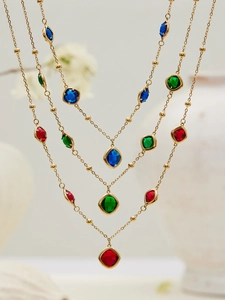 Detail view of gold beaded necklaces featuring faceted red, green, and blue glass gemstones
