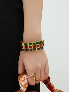 Dettaglio di un bracciale rigido dorato 18k con tre file di pietre preziose colorate quadrate