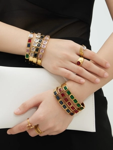 Dettaglio di bracciali in acciaio dorato con pietre colorate dal taglio a smeraldo