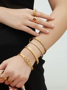 Detail van gestapelde 18k vergulde armbanden en ringen met rode edelsteen en zirkonia