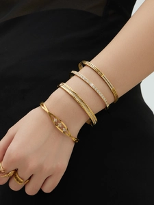 Detailopname van gestapelde gouden armbanden met zirkonia-inleg en geometrische texturen