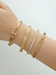 Detail van vier vergulde roestvrijstalen armbanden met zirkonia aan een pols
