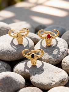 Dettaglio di anelli a testa di toro placcati in oro 18k con pietre rosse e nere su ciottoli